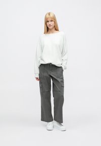 Világosszürke, bő fazonú pulóver bordázott mandzsettákkal, laza, sötétszürke rakott zsebes nadrággal párosítva. Fehér tornacipővel egészül ki a megjelenés.