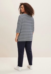 Gestreiftes Hemd mit Dreiviertelärmeln in Marineblau und Weiß. Kombiniert mit marineblauen Hosen und weißen Schuhen, mit einem lockeren Schnitt und weichem Stoff.