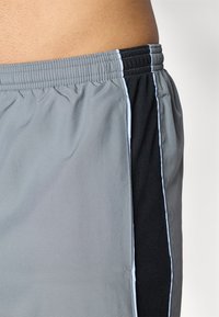 Heren sportshorts van grijze stof met zwarte mesh accenten en witte piping, elastische tailleband en een losse pasvorm.