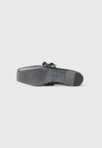 Semelle de chaussure noire avec un design plat, présentant des rainures horizontales pour l'adhérence. Détails décoratifs de sangle en haut avec une finition lisse.