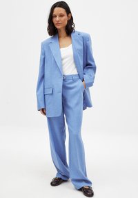 Costume sur mesure bleu clair composé d'un blazer ample à un bouton et de pantalons à jambes larges, fabriqué en tissu texturé.