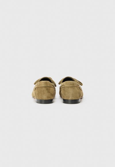 Mocasines de ante en verde oliva con una textura suave, forma redondeada y suelas de goma negra. Presentan correas traseras y un diseño minimalista.