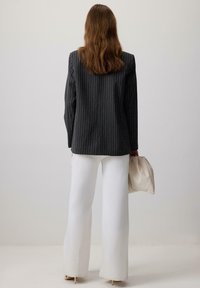 Zwarte pinstriped blazer, lange witte wijde broek en een beige clutch. Gladde textuur, aangesloten schouders en een getailleerd ontwerp.