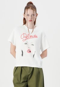 White cotton t-shirt with a cropped design, featuring a graphic of a face and the word "Blondie" in red script. Loose fit, short sleeves.