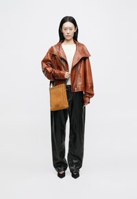 Brun skinnjakke med bred krage, kremfarget genser, svarte skinnbukser og en beige veske med nagler, med skulderreim.