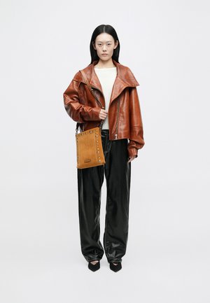 Giacca in pelle marrone con ampio colletto, maglione crema, pantaloni in pelle nera e una borsa beige con borchie, dotata di tracolla.