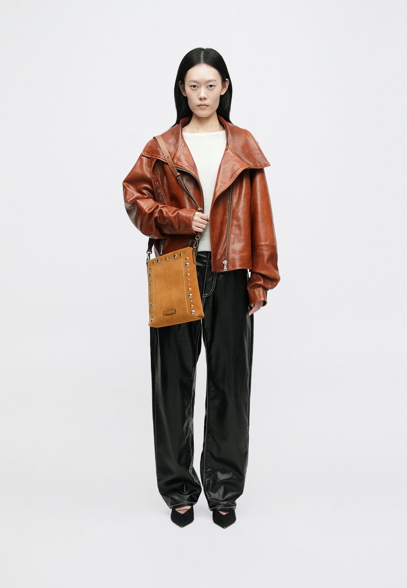 Pruun nahkjakk laiade kraega, kreemjas kampsun, mustad nahkpüksid ja kõikuv pruun kott, millel on nurgad, koos õlavarrega.