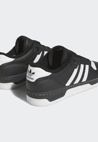 Baskets Adidas noir et blanc avec trois bandes blanches, lacets noirs et logo Adidas sur le talon et la semelle, vues de dos et de côté.