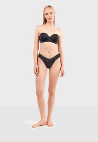 Sujetador negro sin tirantes con tela suave y copas moldeadas, combinado con bragas de bikini negras con encaje en los bordes en forma de V. Sin herrajes visibles.
