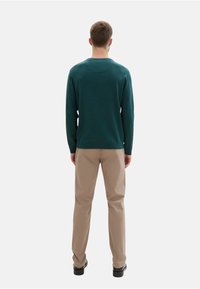 Pull en maille bleu canard avec un col rond, associé à un pantalon beige. La tenue présente un design simple et décontracté ainsi qu'un tissu texturé.
