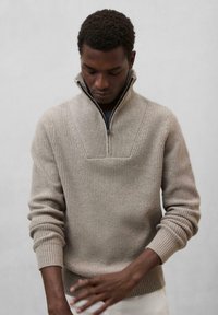 Beige gerippter Strickpullover mit hohem Kragen und halbem Reißverschluss. Verfügt über ein strukturiertes Design und eng anliegende Bündchen.