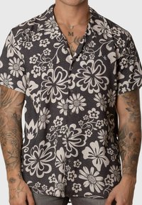 Camisa de manga corta en tejido oscuro con un gran patrón floral blanco. Presenta un cuello con solapa y botones. Material texturizado.