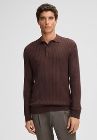Brauner gestrickter Polo-Pullover mit gerippter Textur, kurzem Kragen und drei Knöpfen. Figurbetontes Design mit langen Ärmeln und gerippten Bündchen.