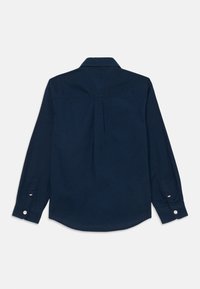 Camisa de manga longa azul-escura com costas em yoke, punhos com botão e bainha curva. Feita de algodão com uma textura suave.