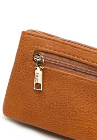 Pochette in pelle texturizzata marrone con dettaglio della cerniera dorata. Presenta un piccolo scomparto frontale con chiusura a zip. Forma compatta e rettangolare.