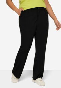 Pantaloni neri in tessuto liscio, con tasche frontali, chiusura a bottone e gamba dritta. Abbinati a sneakers bianche.
