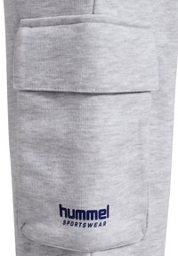 Grijze sweatpants van zacht materiaal met een grote zijzak. Bevat een blauw "hummel SPORTSWEAR" logo nabij de zoom. Casual ontwerp.