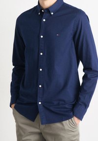 Chemise bleu marine à boutons en coton, dotée d'un col classique et de boutons blancs. Logo présent sur la poitrine gauche.