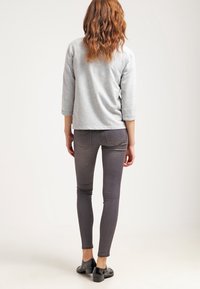 Top gris de manga tres cuartos combinado con vaqueros ajustados gris oscuro. El conjunto presenta una textura suave y un diseño minimalista. Zapatos negros completan el look.
