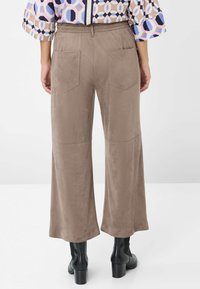 Wijdvallende broeken van zacht, taupe suede-achtig materiaal, met twee achterzakken en een elastische tailleband, gecombineerd met zwart enkellaarzen.