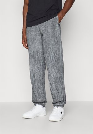 Pantalones jogger grises, ligeros, con textura arrugada, puños elásticos y bolsillos laterales. Combinados con zapatillas blancas.