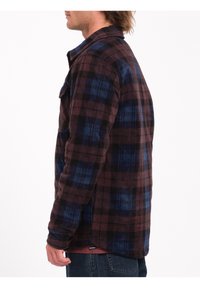 Flannel skjorte i mørkeblå og maroon ternet mønster. Har en frontlomme, lange ærmer og en afrundet bund, lavet af blødt stof.