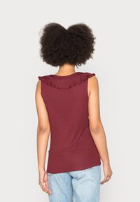Top senza maniche color bordeaux con scollatura arricciata, texture a coste aderente e un semplice design sul retro, abbinato a jeans azzurri chiari.