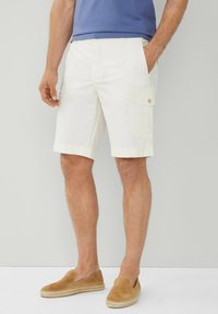 Pantaloni cargo bianchi con tasche laterali, davanti piatto e passanti per cintura. Il tessuto è leggero e dal tocco morbido. Abbinati a scarpe beige slip-on.