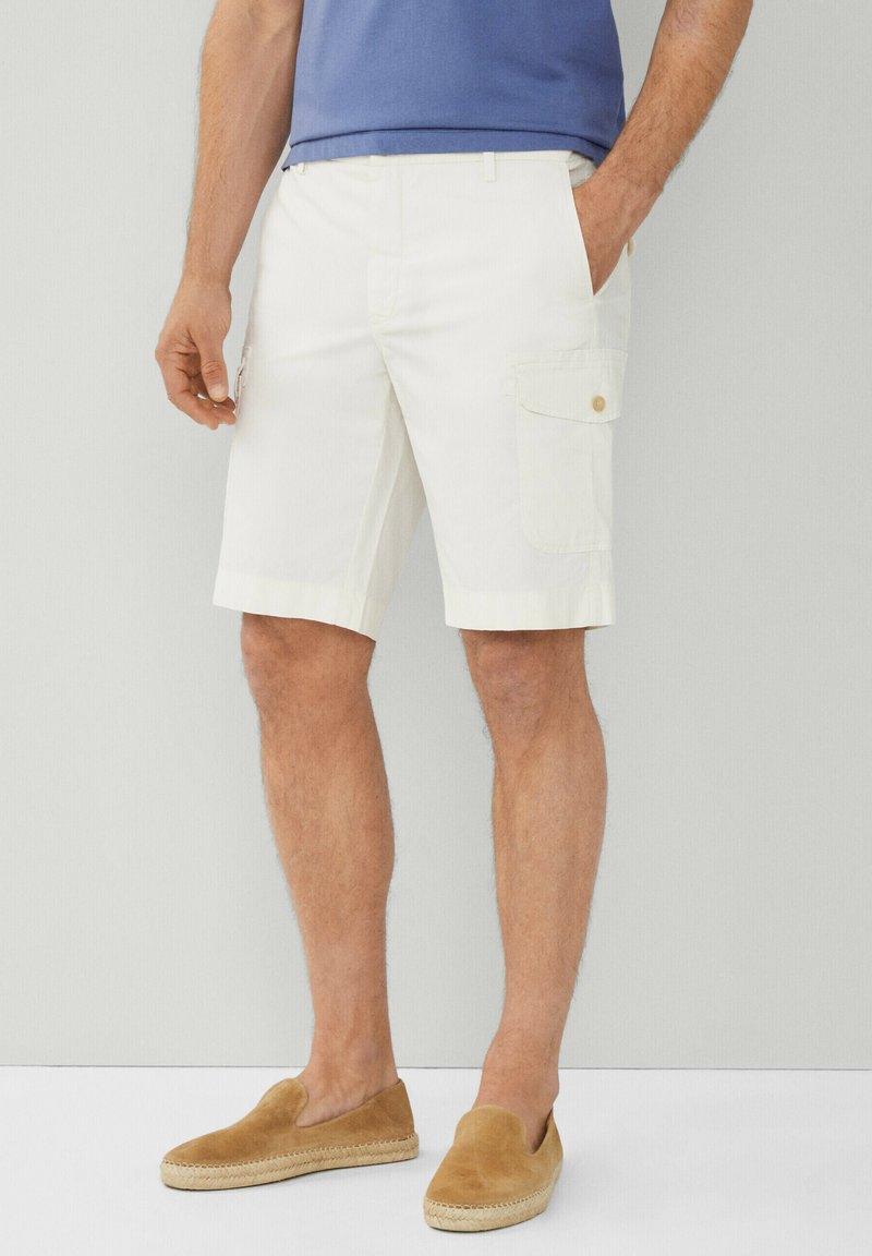 Pantaloni cargo bianchi con tasche laterali, davanti piatto e passanti per cintura. Il tessuto è leggero e dal tocco morbido. Abbinati a scarpe beige slip-on.