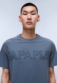 Šedé tričko s krátkým rukávem, zdobené embosovaným nápisem "NAPAPIJR" vpředu. Vyrobeno z měkké bavlny, s kulatým výstřihem a hladkou texturou.