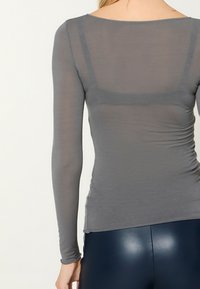 Long-sleeve top in light gray, made from a thin, soft fabric. Features a scoop neckline and subtle gathering at the sides.