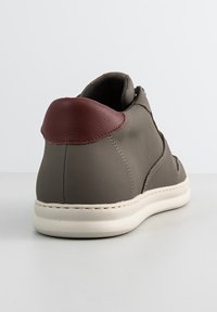 Grå lädersneaker med en vinröd hälaccent, rund form, låg profil och vit gummisula. Slät textur och sydda detaljer.