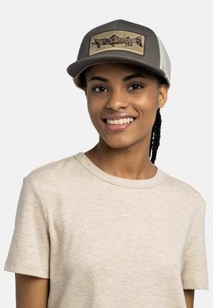 Persona joven sonriendo, con una camiseta beige de cuello redondo y una gorra de malla gris con un parche que muestra un diseño estilizado de pez.