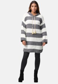 Paski oversize bluza z kapturem w białej i szarej dzianinie z sznurkiem i frędzlami; zestawiona z wąskimi czarnymi dżinsami i czarnymi botkami za kostkę.