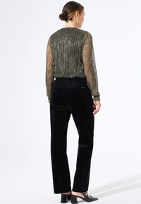 Blusa verde olivo transparente con pliegues verticales, combinada con pantalones de pana negros de cintura alta y zuecos negros de tacón.