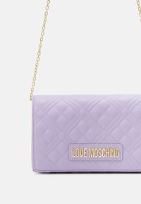 Lavendel quiltad väska med guld kedjeaxelrem och en guldplakett med texten "LOVE MOSCHINO" på framsidan.