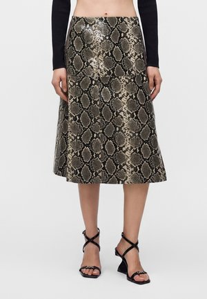 Jupe mi-longue avec motif peau de serpent marron et noir, portée avec un top noir à manches longues et des sandales noires à talons avec lanières.