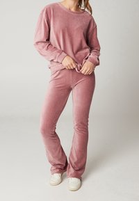 Sada pohodlného oblečení skládající se ze dvou kusů v měkké, popelavě růžové rib rovné látce; obsahuje volný top s dlouhým rukávem a kulatým výstřihem a rozšířené kalhoty.
