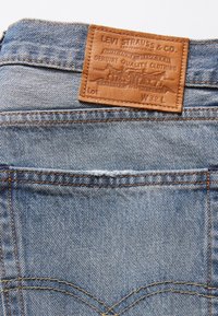 Levi's farkkut liivit ovat vaaleansinisiä, ja niissä on nahkainen etiketti, jossa on merkin tiedot ja kulunut pinta. Korostettu kontrastivärisillä ompeleilla.
