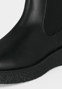 Gros plan d'une botte Chelsea en cuir noir avec semelle en caoutchouc texturée et panneau latéral élastique.