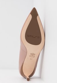 Semelle en cuir d'une chaussure beige à bout pointu, marque "Unisa", taille 37, avec une inscription "Made in Spain", sur un fond blanc en coin.
