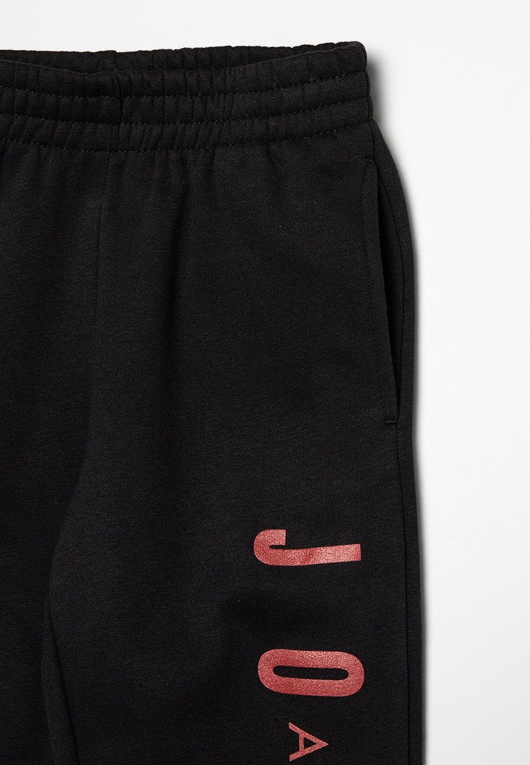 Pantaloni della tuta neri con vita elasticizzata, tasche laterali e scritte in metallo rosso che formano la parola "JOA" sulla gamba sinistra. Tessuto morbido.