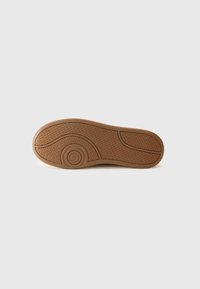 Semelle de chaussure en caoutchouc tan avec des motifs texturés, un design courbé et un logo. Bords lisses et périmètre renforcé pour la durabilité.