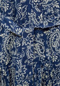 Modrá šaty s vzorem obsahujícím paisley design v bílé barvě, vyrobené z texturované látky, s předním zapínáním na knoflíky a detailem nařaseného pasu.