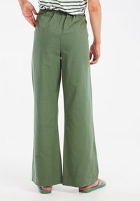 Groene wijde broek met een elastische tailleband en een gladde textuur. De zoom is recht en de stof lijkt lichtgewicht en ademend te zijn.