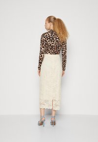 Langermet topp med leopardmønster kombinert med en kremfarget midi-skjørt i blonder med bølget kant og sliss bak, accessorert med blå hælsandaler.