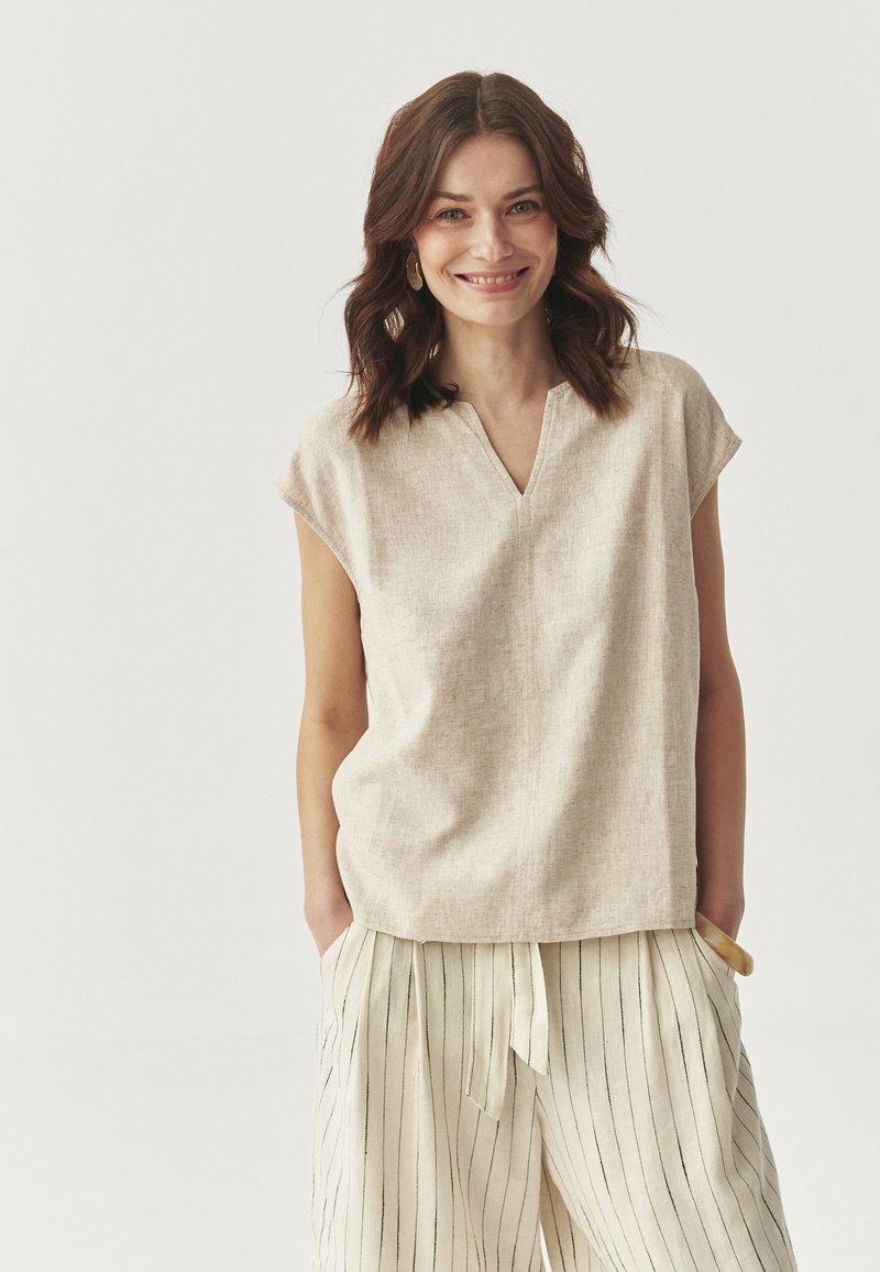 Top beige in lino con scollo a V e maniche a cappuccio, caratterizzato da una vestibilità rilassata. Abbinato a pantaloni a gamba larga a righe di colore crema.