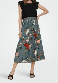 Floral midi-nederdel i teal stof med røde og hvide blomster, høj talje med et bundet bælte, parret med en sort volangtop og sorte sandaler.