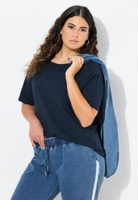 Námořnická modrá tričko s krátkým rukávem s textem "TRUE", doplněné světle modrými džíny typu joggers se elastickým pasem a bočními pruhy.