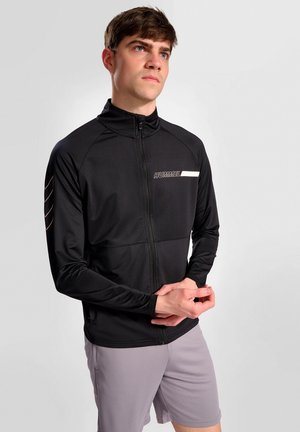 Zwarte sportjas met hoge kraag, lange mouwen en een rits aan de voorkant. Heeft een witte horizontale streep en logo op de borst.
